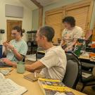 Three young people at a table, with microscopes and large books open on the table. An older man sits with them.